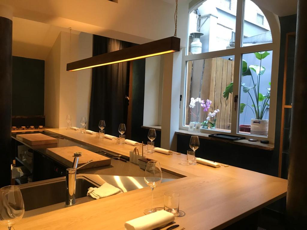 Une vue de l'intérieur d'une cuisine élégante avec un bar en bois, des verres à vin et des serviettes blanches, donnant sur une cour avec des plantes et des fleurs.