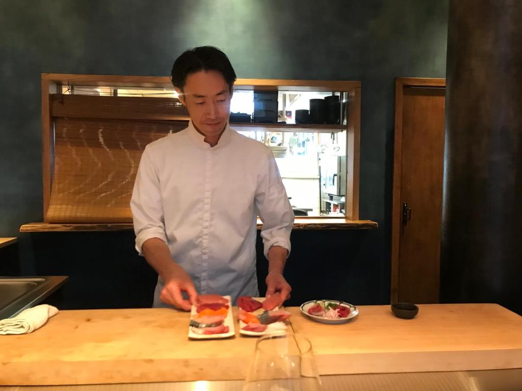 Un chef en tenue blanche prépare des plats avec du poisson frais sur un comptoir en bois, dans un cadre de restaurant.