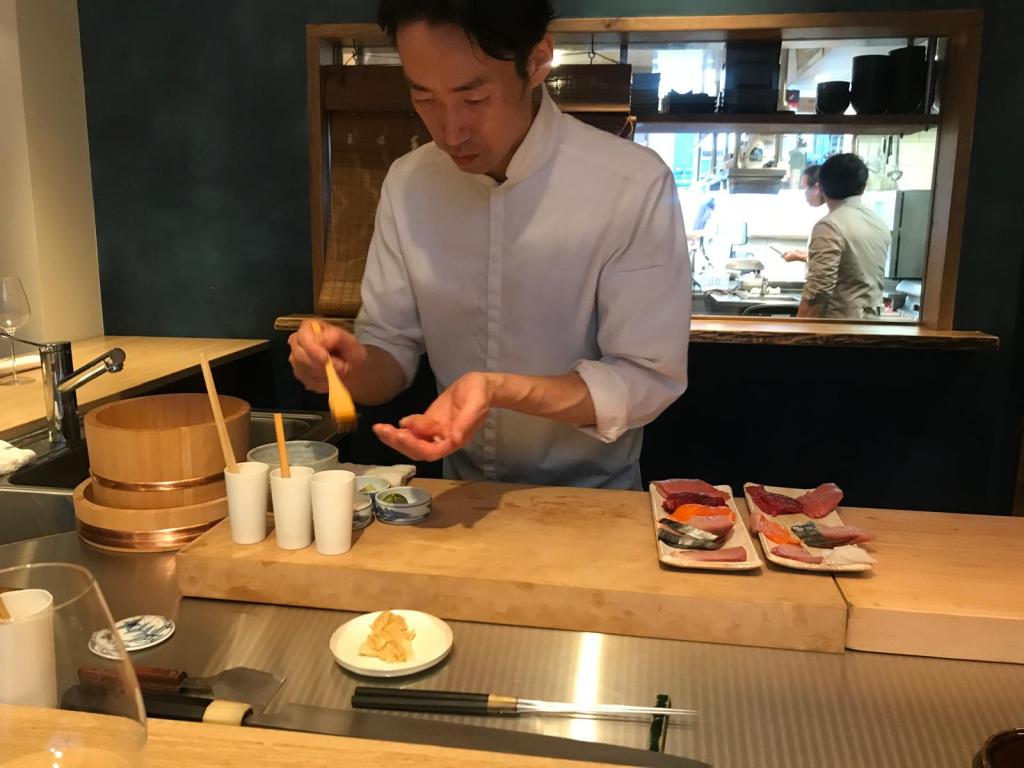 Un chef préparant des plats de sushi dans un restaurant japonais, avec des assiettes de sashimi et divers condiments sur le comptoir.